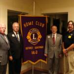 Gathered around the Banner are Lion Lou Danese, IPDG Steve Benedict, DG Jim Bolin and Lion President John Leed